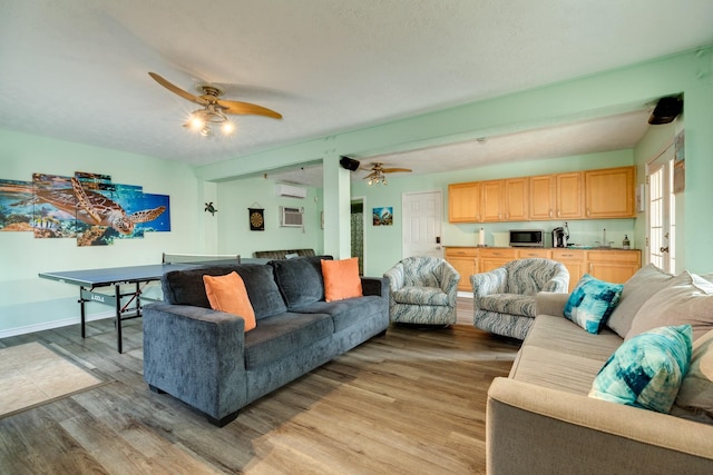 living room with ceiling fan, a wall mounted air conditioner, light wood-style flooring, and baseboards