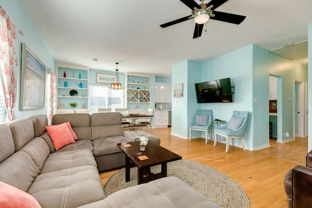 living area with attic access, light wood-type flooring, baseboards, and a ceiling fan