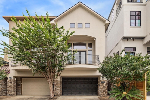 view of front of property with an attached garage, a balcony, stone siding, driveway, and stucco siding