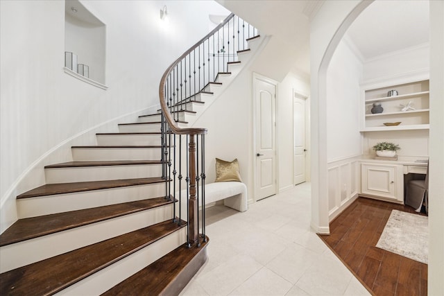 stairway featuring built in features, arched walkways, a decorative wall, ornamental molding, and wood finished floors