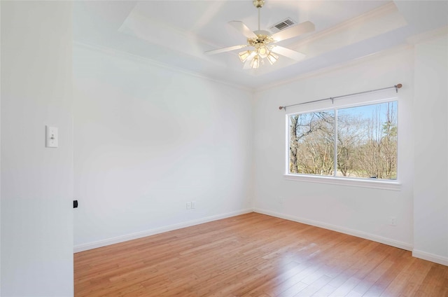 empty room featuring light wood-style flooring, crown molding, a tray ceiling, and baseboards