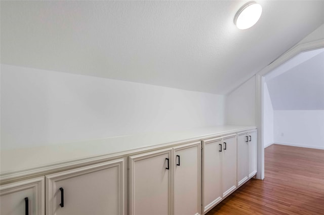 bonus room with light wood finished floors, baseboards, vaulted ceiling, and a textured ceiling