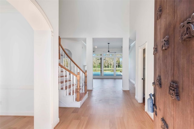 entrance foyer with baseboards, a towering ceiling, light wood finished floors, and stairs