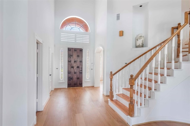 foyer entrance featuring visible vents, a towering ceiling, wood finished floors, baseboards, and stairs