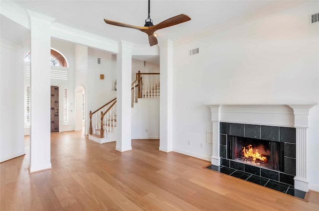 unfurnished living room featuring a tile fireplace, wood finished floors, visible vents, baseboards, and stairs