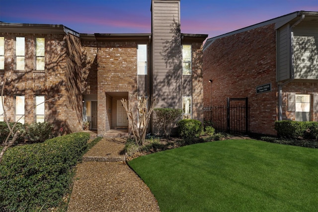 view of property with brick siding, a lawn, and a chimney