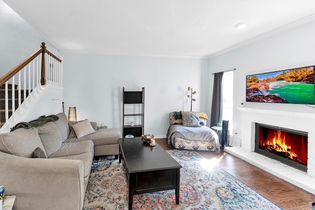 living room with a brick fireplace, crown molding, stairs, and wood finished floors