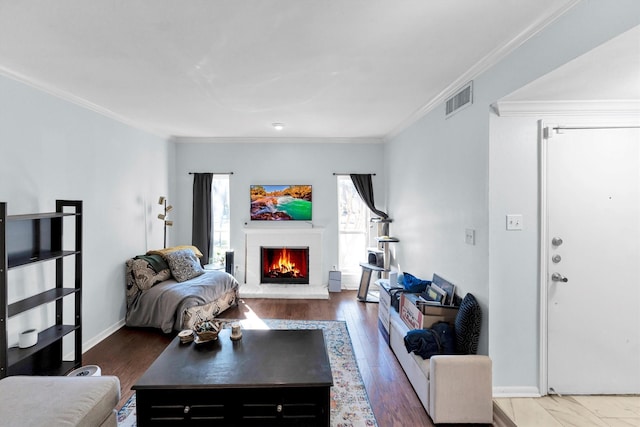 living room with a fireplace, wood finished floors, visible vents, baseboards, and ornamental molding