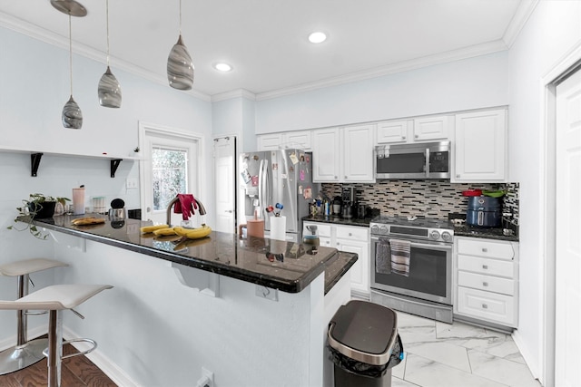 kitchen with a peninsula, ornamental molding, appliances with stainless steel finishes, dark countertops, and a kitchen bar