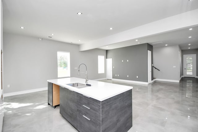 kitchen featuring a sink, baseboards, an island with sink, plenty of natural light, and modern cabinets