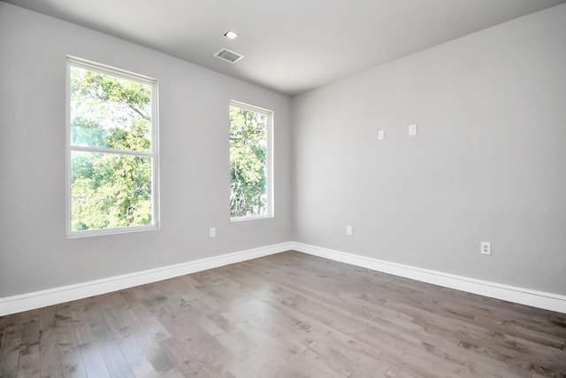 spare room featuring a healthy amount of sunlight, visible vents, baseboards, and wood finished floors