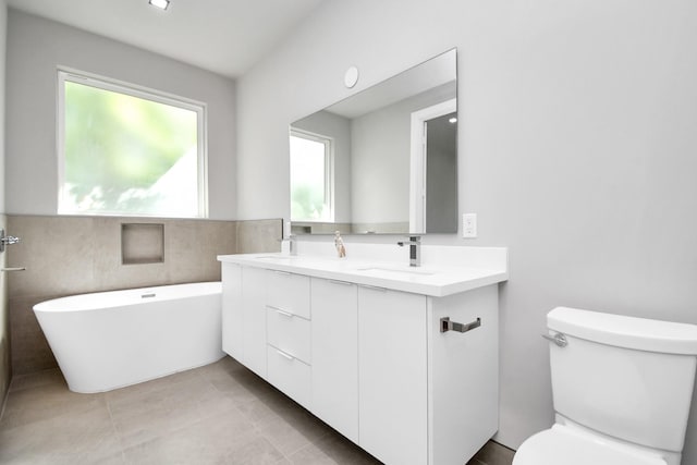 bathroom with double vanity, a freestanding bath, toilet, a sink, and tile patterned flooring