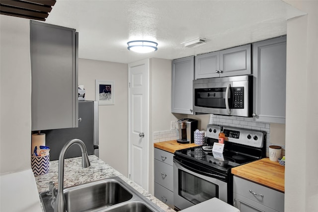 kitchen with gray cabinetry, butcher block countertops, a sink, visible vents, and appliances with stainless steel finishes