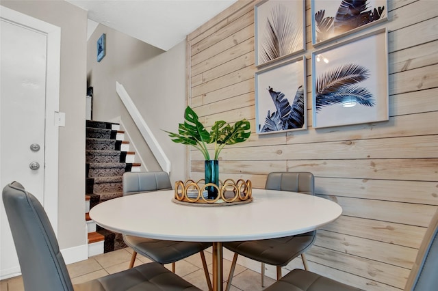 tiled dining room featuring wooden walls and stairs