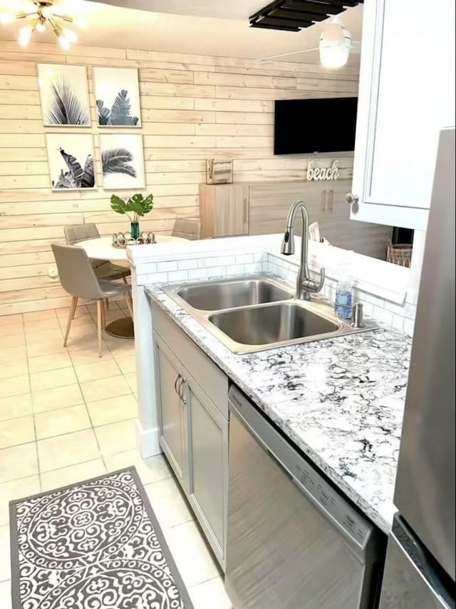 kitchen with light stone counters, stainless steel appliances, light tile patterned flooring, a sink, and wood walls