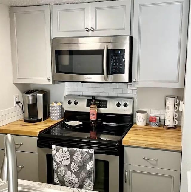 kitchen with appliances with stainless steel finishes, butcher block counters, and backsplash