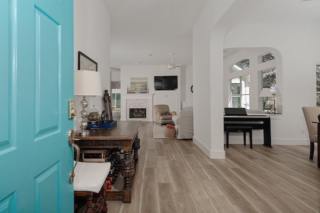 foyer entrance with light wood finished floors, baseboards, arched walkways, a glass covered fireplace, and a ceiling fan