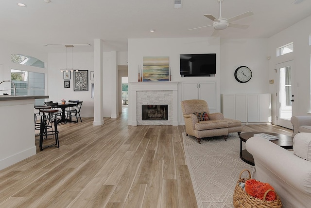 living room with a stone fireplace, a wealth of natural light, light wood finished floors, and ceiling fan