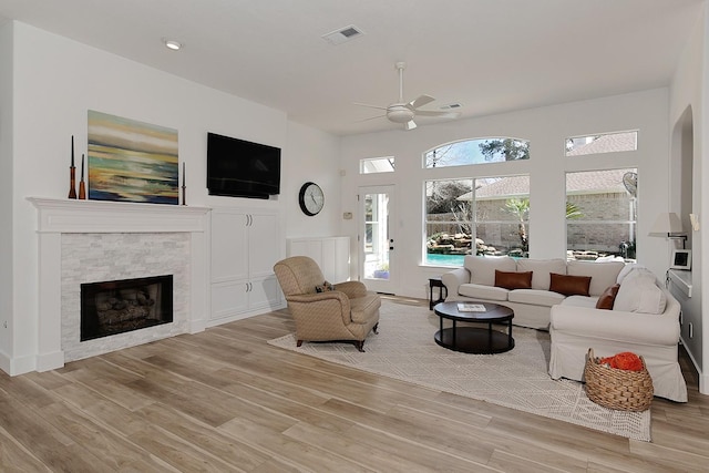 living room featuring visible vents, a fireplace, a ceiling fan, and light wood finished floors