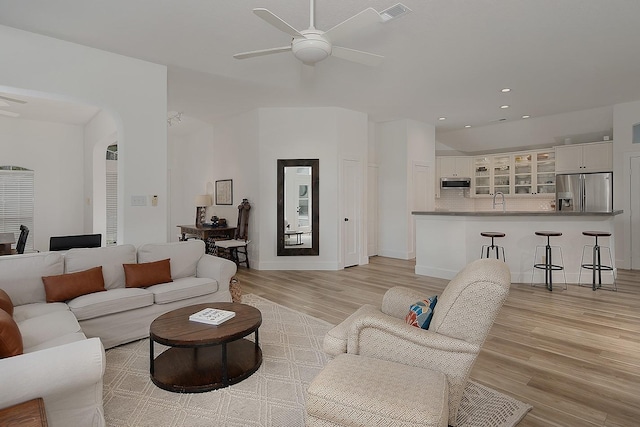 living area with light wood finished floors, visible vents, arched walkways, and ceiling fan