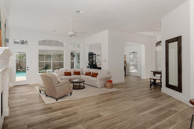 living area with a ceiling fan, visible vents, arched walkways, and light wood finished floors