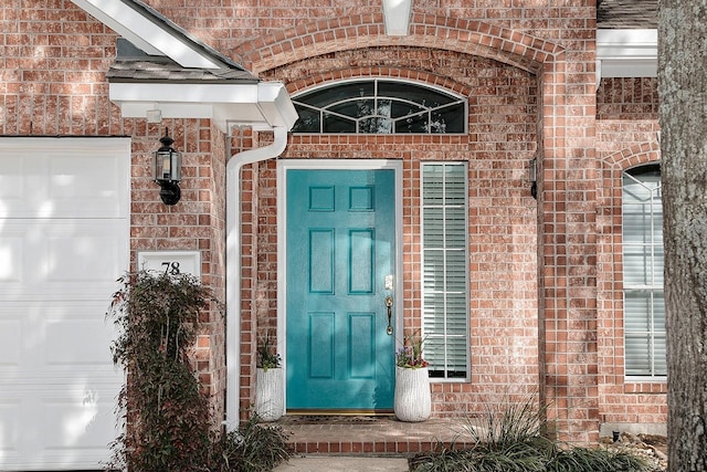 view of exterior entry with brick siding and an attached garage