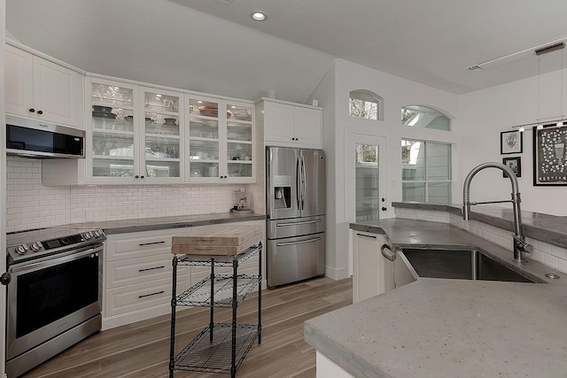 kitchen with a sink, stainless steel appliances, glass insert cabinets, white cabinetry, and tasteful backsplash