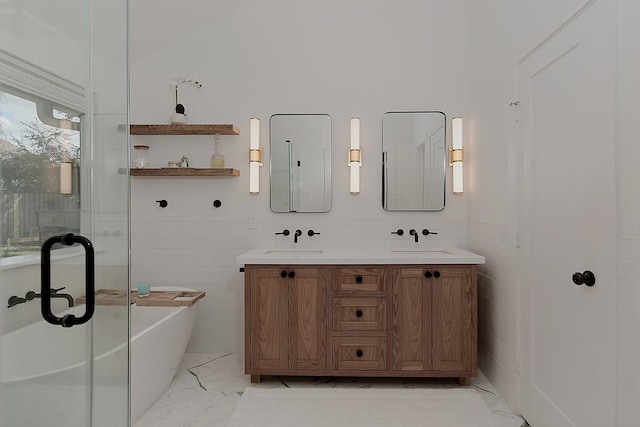 full bath featuring a soaking tub, marble finish floor, tile walls, and a sink