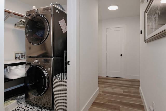 laundry area featuring laundry area, wood finished floors, baseboards, and stacked washer and dryer