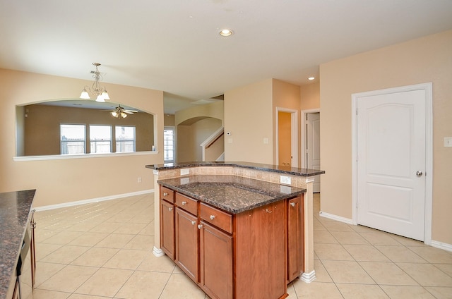 kitchen featuring dark stone counters, a kitchen island, light tile patterned flooring, pendant lighting, and ceiling fan with notable chandelier