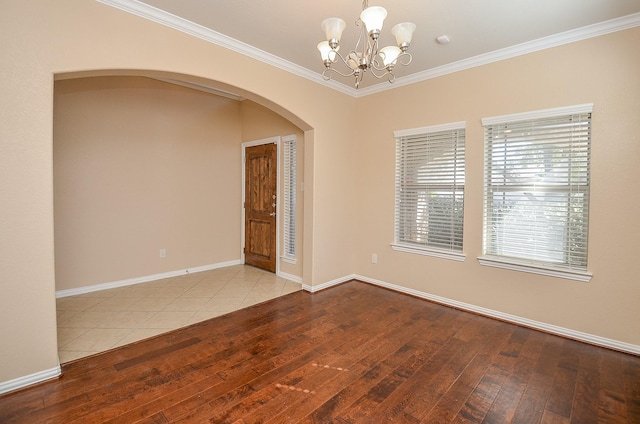 spare room with arched walkways, crown molding, baseboards, wood-type flooring, and an inviting chandelier