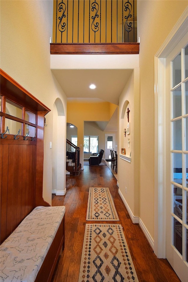 hallway with baseboards, stairs, arched walkways, and hardwood / wood-style floors