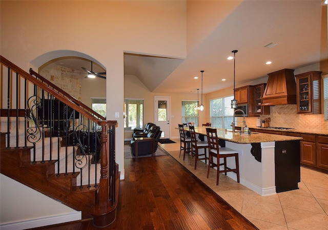 kitchen with light stone counters, premium range hood, backsplash, an island with sink, and a kitchen bar