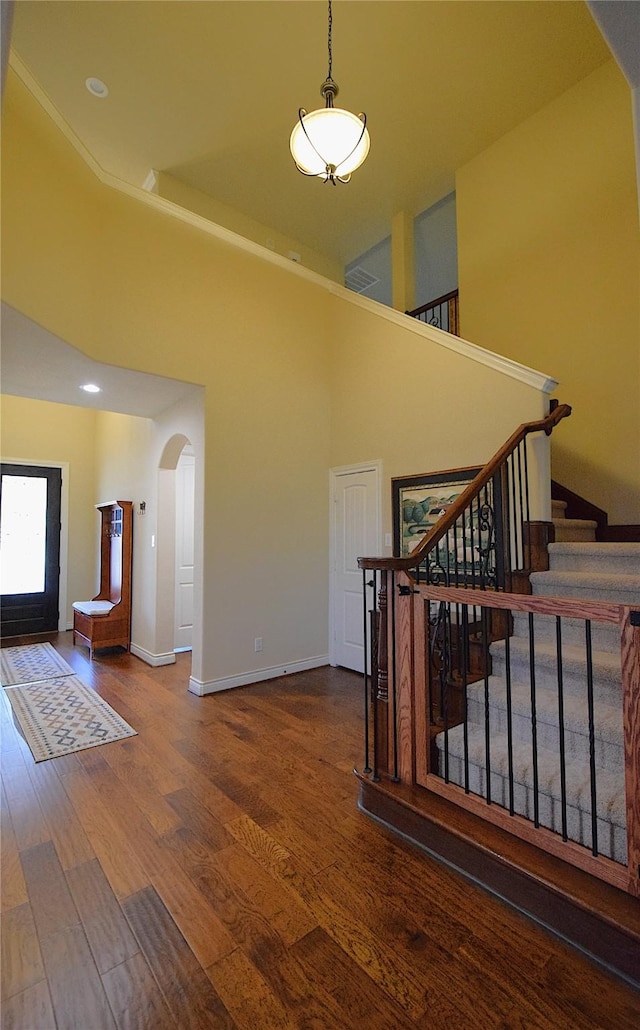 interior space featuring a towering ceiling, baseboards, arched walkways, and wood finished floors