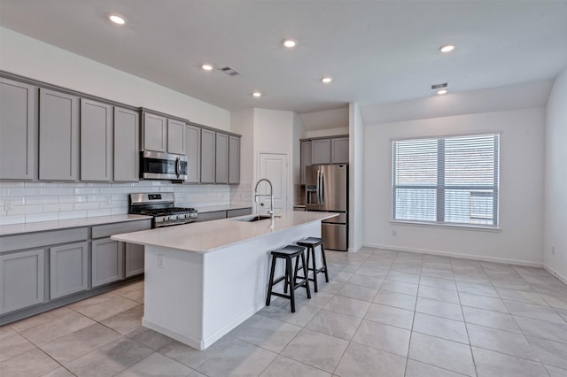 kitchen with an island with sink, a breakfast bar, gray cabinets, stainless steel appliances, and a sink