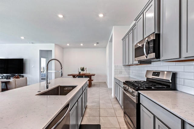 kitchen featuring a sink, light stone countertops, stainless steel appliances, gray cabinetry, and backsplash