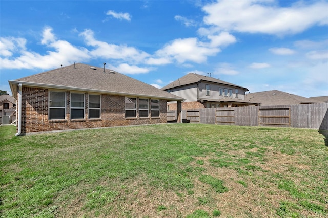 back of house with a yard, a fenced backyard, a shingled roof, and brick siding