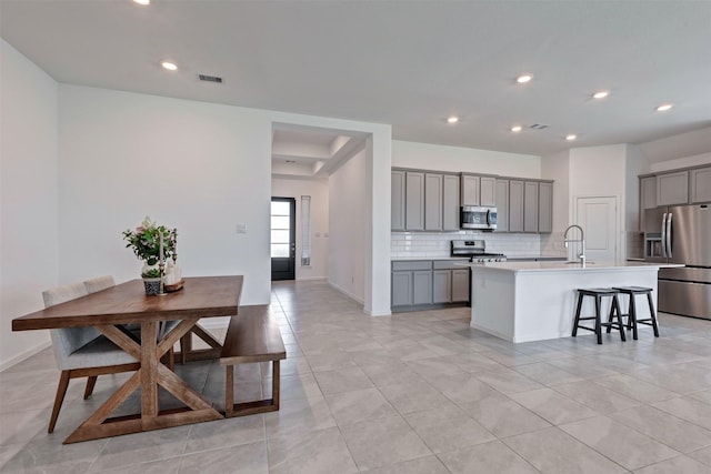 kitchen featuring tasteful backsplash, visible vents, appliances with stainless steel finishes, gray cabinetry, and a sink