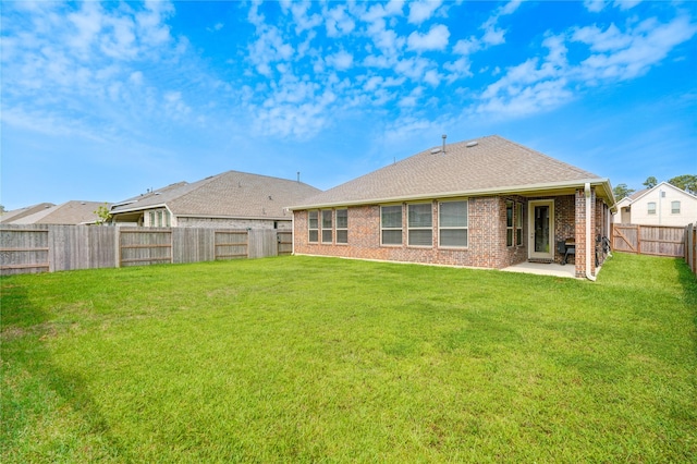 rear view of house with a shingled roof, a fenced backyard, a yard, a patio area, and brick siding