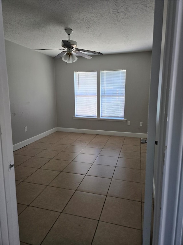 empty room with ceiling fan, a textured ceiling, baseboards, and tile patterned floors