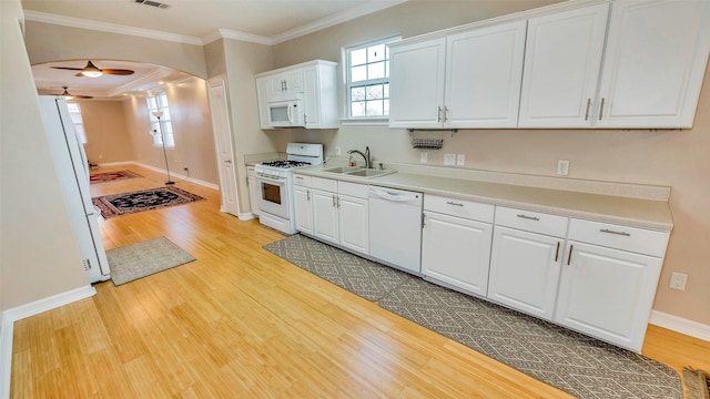 kitchen featuring white appliances, arched walkways, ornamental molding, light wood-type flooring, and a sink