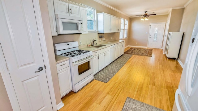 kitchen featuring light countertops, ornamental molding, white cabinets, a sink, and white appliances