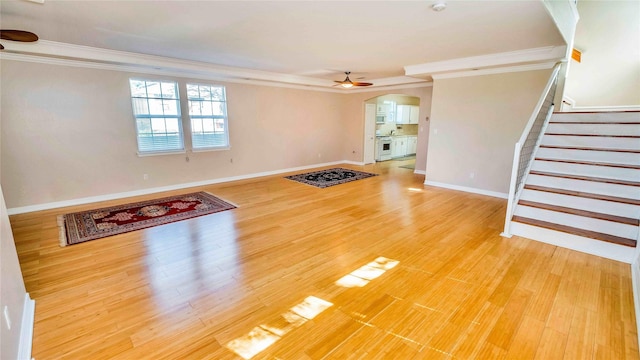 unfurnished living room with arched walkways, a ceiling fan, light wood-style flooring, stairs, and crown molding