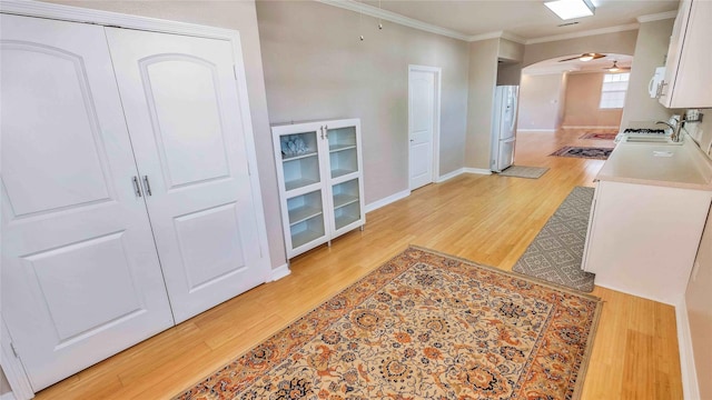 kitchen featuring arched walkways, light wood-style flooring, white appliances, a sink, and crown molding