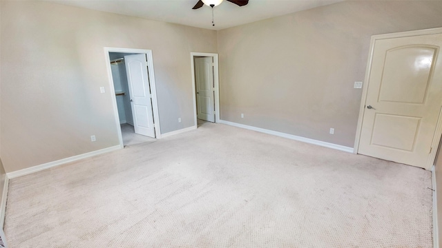 unfurnished bedroom featuring a ceiling fan, a walk in closet, light colored carpet, and baseboards