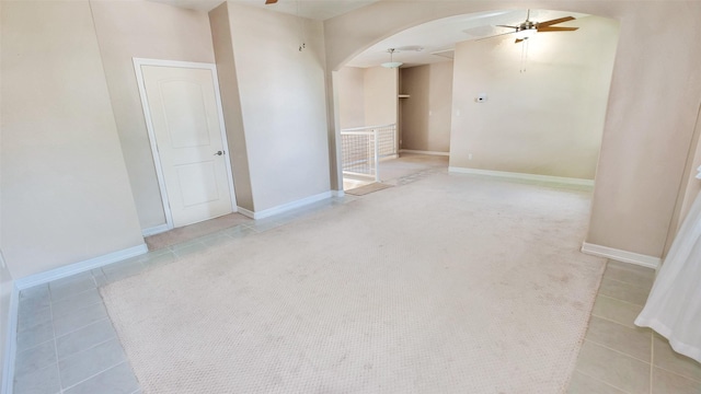 tiled empty room with arched walkways, carpet flooring, a ceiling fan, and baseboards