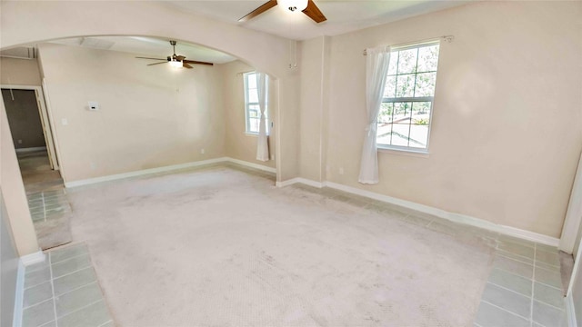 carpeted empty room with a wealth of natural light, arched walkways, and a ceiling fan