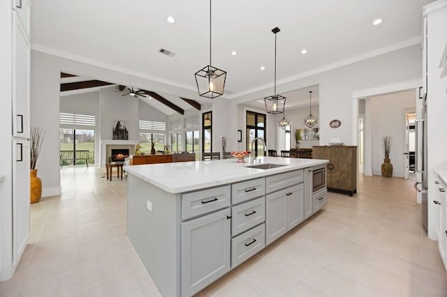 kitchen with vaulted ceiling with beams, visible vents, a ceiling fan, a sink, and a warm lit fireplace