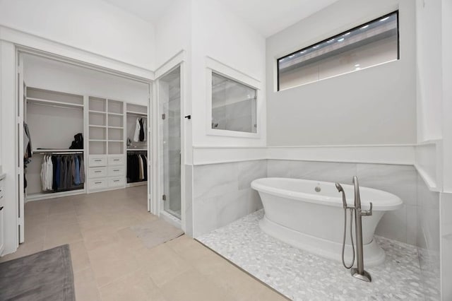 bathroom with a freestanding tub, tile patterned flooring, wainscoting, a shower stall, and a walk in closet