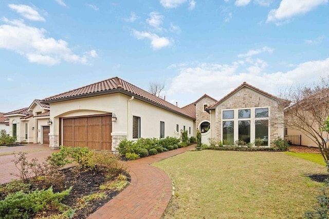 mediterranean / spanish home with an attached garage, stone siding, a tile roof, and a front yard